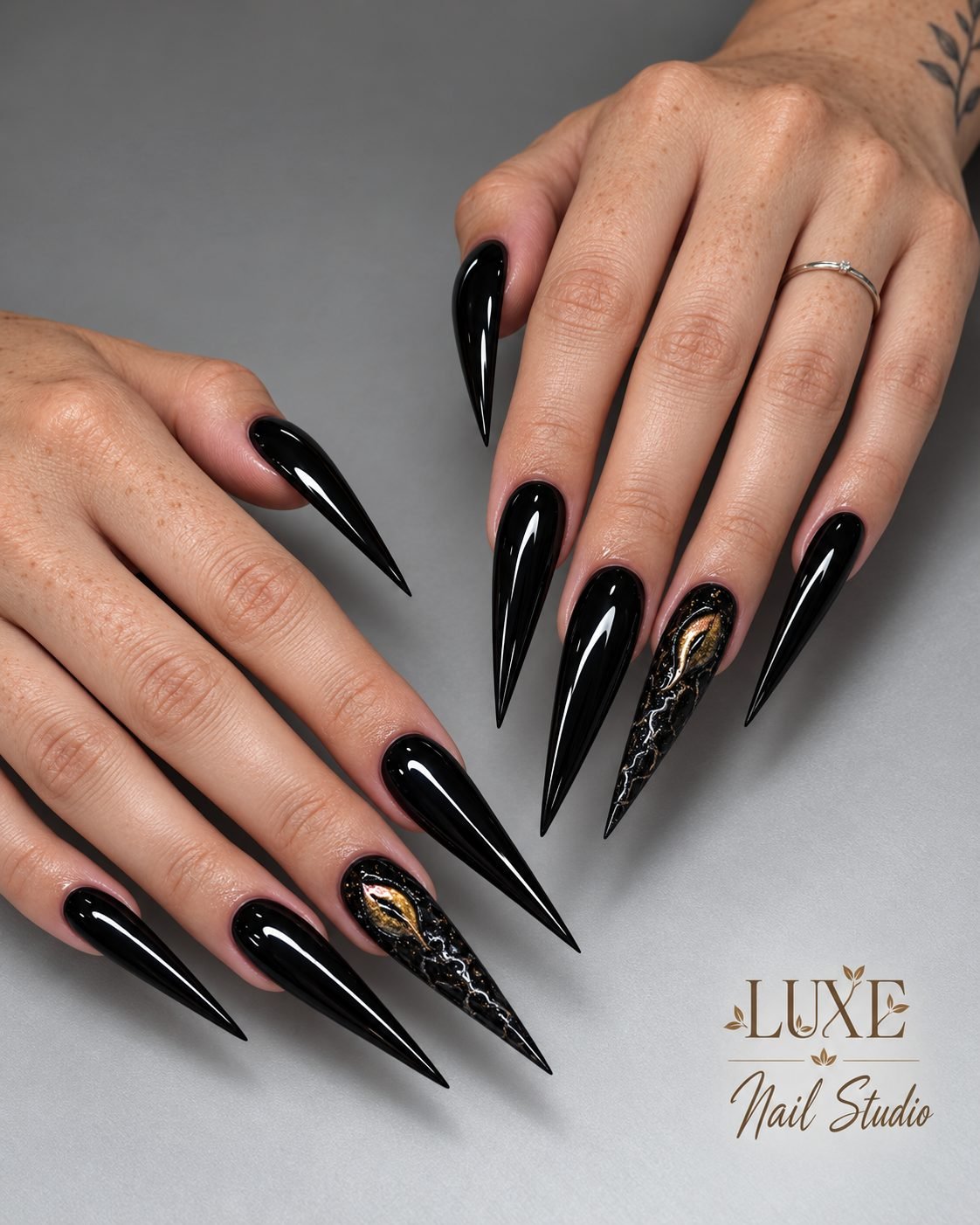 Glossy black stiletto nails with a gold leaf and marble accent by Luxe Nail Studio