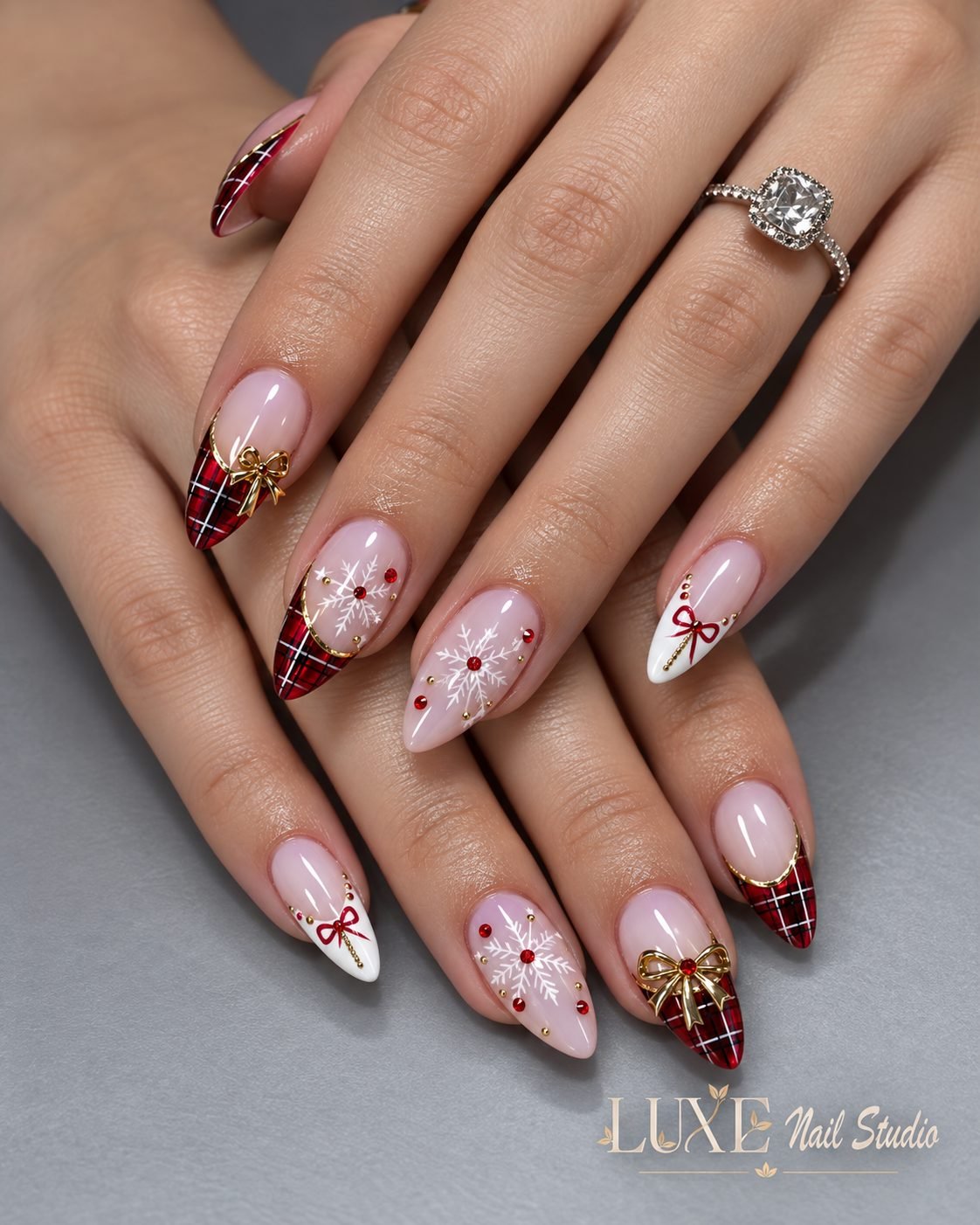 Pink almond nails with red plaid tips, snowflakes, and gold bows by Luxe Nail Studio